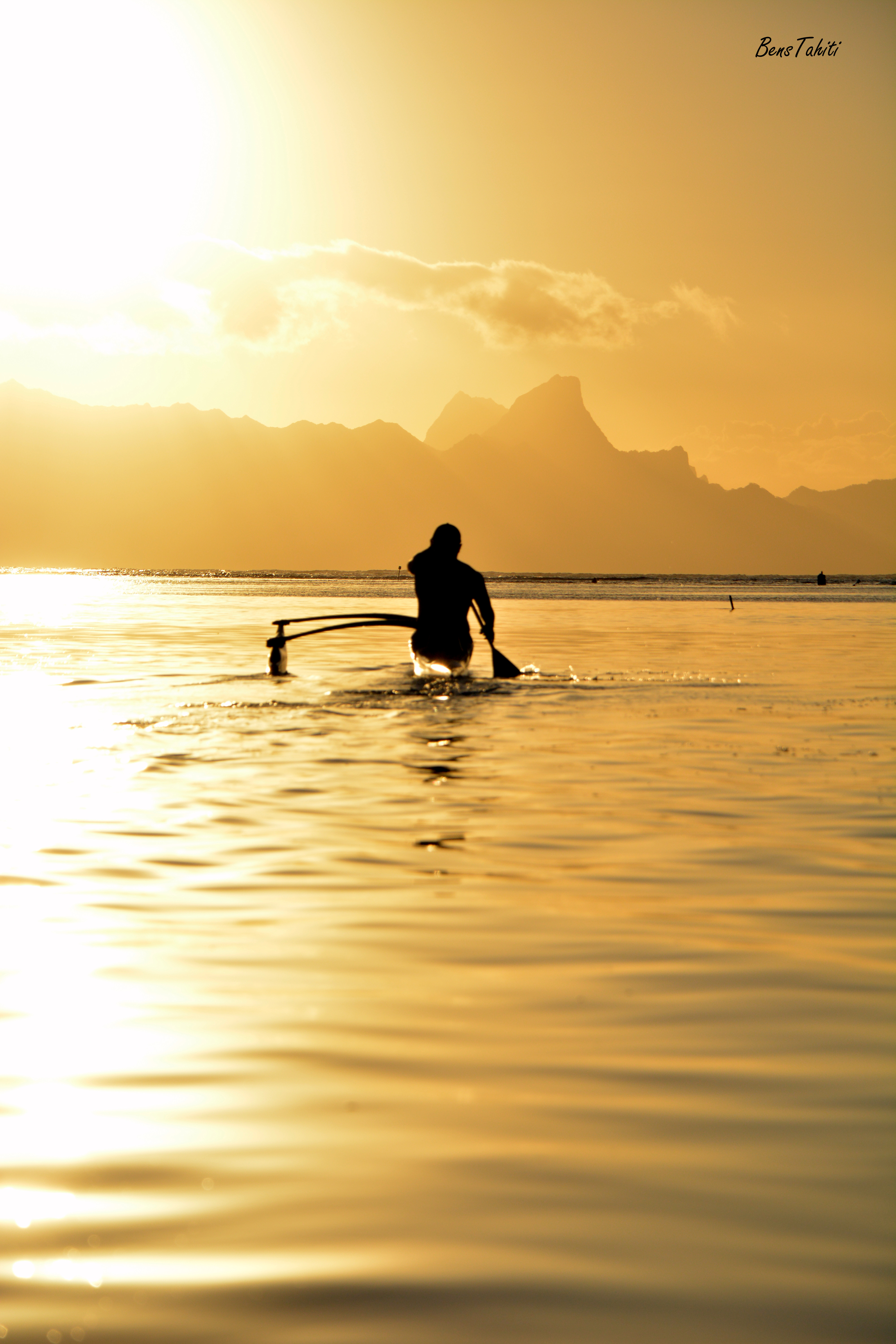 Une silhouette et sa pirogue sur le lagon dans une lumière dorée, par Bens Tahiti