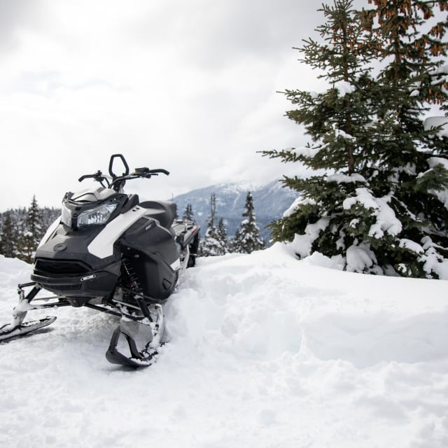 A snowmobile parked on a snowy trail surrounded by evergreen trees and scenic mountains