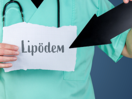 Ein Arzt in grüner Kleidung hält ein Blatt Papier mit dem Schriftzug "Lipödem" und zeigt mit einem schwarzen Pfeil darauf. Das Bild hebt das Thema Lipödem hervor, möglicherweise im Zusammenhang mit einer ärztlichen Beratung.