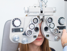Frau bei augenärztlicher Sehstärkenmessung mit Phoropter während einer professionellen Augenuntersuchung in der Praxis, Arzt stellt die Linsen zur Bestimmung der optimalen Sehkorrektur ein.