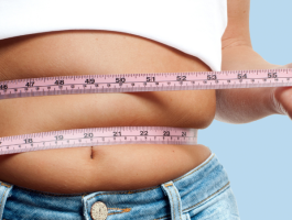 Frau misst ihren Bauchumfang mit einem Maßband um die Taille – Symbolbild für Übergewicht, Gewichtszunahme und mögliche Ursachen wie Ernährung, Bewegungsmangel oder Lebensstil.