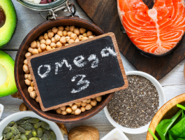 Lebensmittel mit Omega-3-Fettsäuren wie Lachs, Avocado, Nüsse, Eier, Spinat, Chiasamen und Leinöl auf einem Holztisch arrangiert.