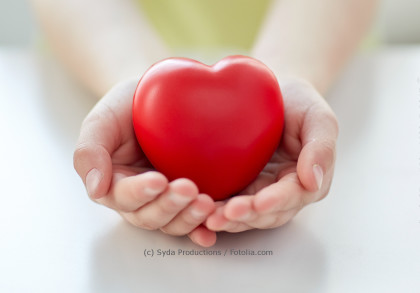 Ein Paar Hände hält ein rotes Herz aus Plastik, das für Liebe und Fürsorge steht.