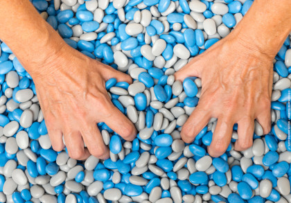 Zwei Hände greifen in einen Haufen bunter Steine mit blauen und grauen Farben.