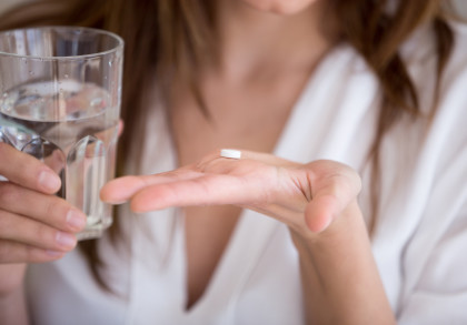 Eine Person hält ein Glas Wasser in der einen Hand und eine weiße Tablette in der anderen Hand.