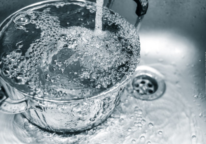 Ein Topf wird mit sprudelndem Wasser aus einem Wasserhahn gefüllt. Das Wasser läuft in einen Edelstahlspülbeckenabfluss.