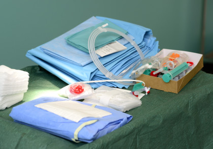 Ein Tisch in einem Operationssaal, bedeckt mit blauen und grünen sterilen Tüchern, medizinischen Schläuchen, Spritzen, Mull und weiteren chirurgischen Instrumenten. Diese Materialien sind sorgfältig organisiert und bereit für eine bevorstehende Operation.