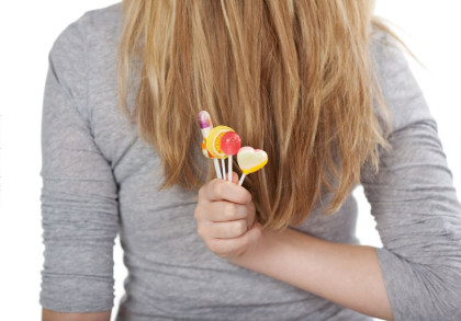 Eine Person mit langen blonden Haaren trägt ein graues Oberteil und hält mehrere bunte Lutscher in der Hand.