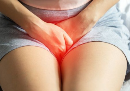 Eine Person sitzt auf einem Bett und hält sich den schmerzenden Unterbauch, der rot hervorgehoben ist. 