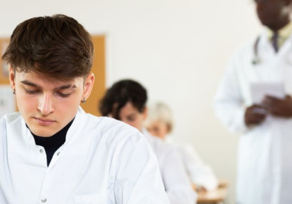 Ärzte in unterschiedlichem Alter sitzen an Tischen in einem Klassenzimmer.