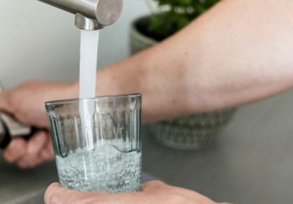 Eine Person füllt ein Glas mit Leitungswasser an einem Wasserhahn in der Küche – Symbolbild für Trinkwasserhygiene und Schutz vor Legionellen im Haushalt.