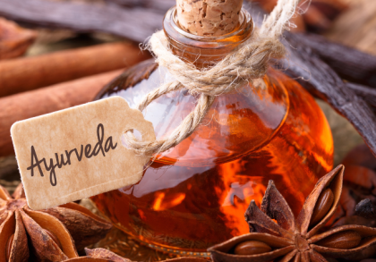 Ayurveda-Fläschchen mit Etikett, umgeben von Zimtstangen, Sternanis, Vanilleschoten und Gewürzen als Symbol für ayurvedische Ernährung und Naturheilkunde.