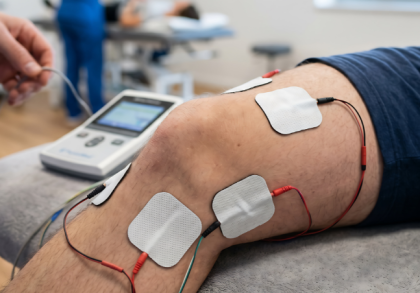 Patient liegt in einer Physiotherapiepraxis auf einer Behandlungsliege, während Elektroden zur Iontophorese am Knie angebracht sind. Die Stromtherapie dient der gezielten Behandlung von Schmerzen, Entzündungen oder Gelenkbeschwerden.