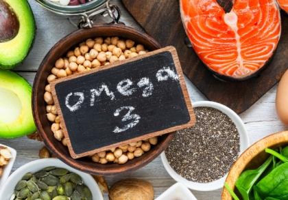 Lebensmittel mit Omega-3-Fettsäuren wie Lachs, Avocado, Nüsse, Eier, Spinat, Chiasamen und Leinöl auf einem Holztisch arrangiert.