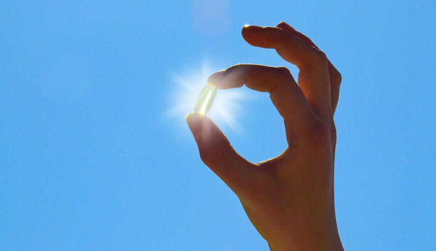 Hand hält Vitamin D Kapsel in den Himmel, die leuchtet wie die Sonne.