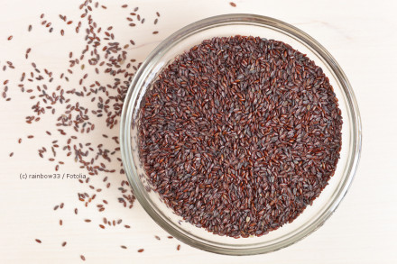 Eine Schale voller dunkler Samen, die auf einem hellen Holzuntergrund steht. Einige Samen sind aus der Schale gefallen und liegen verstreut auf dem Holz.