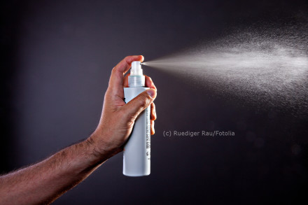 Ein Mensch sprüht eine weiße Flüssigkeit aus einer weißen Sprühflasche. Der Hintergrund ist dunkel.