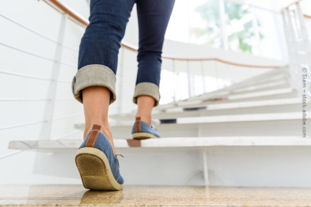 Eine Person mit hochgekrempelten Jeans und blauen Schuhen geht eine weiße Treppe hinauf.
