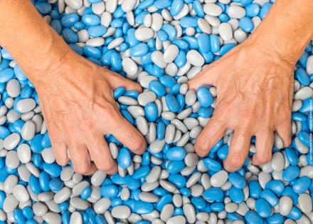 Zwei Hände greifen in einen Haufen bunter Steine mit blauen und grauen Farben.