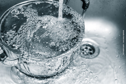 Ein Topf wird mit sprudelndem Wasser aus einem Wasserhahn gefüllt. Das Wasser läuft in einen Edelstahlspülbeckenabfluss.