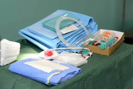 Ein Tisch in einem Operationssaal, bedeckt mit blauen und grünen sterilen Tüchern, medizinischen Schläuchen, Spritzen, Mull und weiteren chirurgischen Instrumenten. Diese Materialien sind sorgfältig organisiert und bereit für eine bevorstehende Operation.