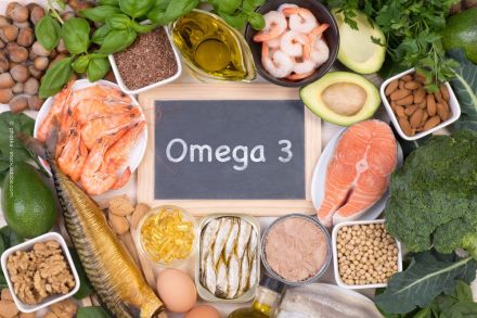 Eine Tafel mit der Aufschrift "Omega 3" steht im Zentrum, umgeben von Lebensmitteln, die reich an Omega-3-Fettsäuren sind, darunter Avocado, Lachs, Krabben, Nüsse, Olivenöl, Fisch, Eier, Walnüsse und grünem Gemüse wie Brokkoli.