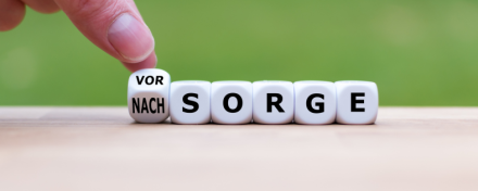 Hand dreht einen Würfel mit den Worten „VORSORGE“ und „NACHSORGE“ auf grünem Hintergrund, um den Fokus auf „VORSORGE“ zu legen. Symbol für Planung und Verantwortung.