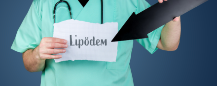 Ein Arzt in grüner Kleidung hält ein Blatt Papier mit dem Schriftzug "Lipödem" und zeigt mit einem schwarzen Pfeil darauf. Das Bild hebt das Thema Lipödem hervor, möglicherweise im Zusammenhang mit einer ärztlichen Beratung.