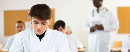 Ärzte in unterschiedlichem Alter sitzen an Tischen in einem Klassenzimmer.