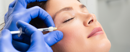 Ärztin injiziert Botulinumtoxin (Botox) mit Spritze in die seitliche Augenregion einer Patientin zur Faltenbehandlung; Nahaufnahme einer ästhetischen Behandlung mit medizinischen Handschuhen.