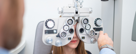 Frau bei augenärztlicher Sehstärkenmessung mit Phoropter während einer professionellen Augenuntersuchung in der Praxis, Arzt stellt die Linsen zur Bestimmung der optimalen Sehkorrektur ein.