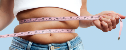 Frau misst ihren Bauchumfang mit einem Maßband um die Taille – Symbolbild für Übergewicht, Gewichtszunahme und mögliche Ursachen wie Ernährung, Bewegungsmangel oder Lebensstil.