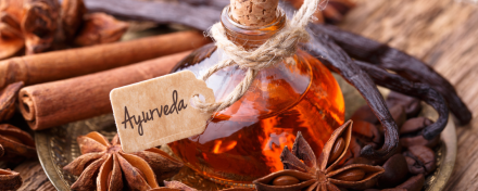 Ayurveda-Fläschchen mit Etikett, umgeben von Zimtstangen, Sternanis, Vanilleschoten und Gewürzen als Symbol für ayurvedische Ernährung und Naturheilkunde.