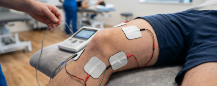 Patient liegt in einer Physiotherapiepraxis auf einer Behandlungsliege, während Elektroden zur Iontophorese am Knie angebracht sind. Die Stromtherapie dient der gezielten Behandlung von Schmerzen, Entzündungen oder Gelenkbeschwerden.