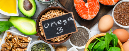 Lebensmittel mit Omega-3-Fettsäuren wie Lachs, Avocado, Nüsse, Eier, Spinat, Chiasamen und Leinöl auf einem Holztisch arrangiert.