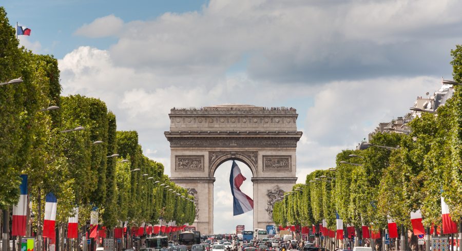 Arc de Triomphe viewed up the Champs Elysees and a large french flag flying under the arch
