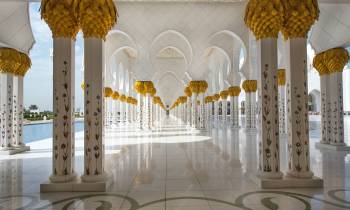 a clock hanging from the ceiling with Sheikh Zayed Mosque in the background