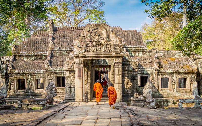 a person standing in front of a stone building with Angkor Wat in the background