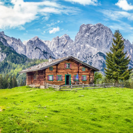 Panoramic view of beautiful mountain scenery in the Alps with traditional rural mountain chalet and fresh green meadows