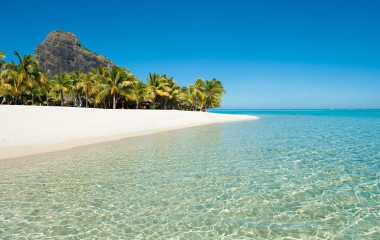 Menschenleerer weißer Sandstrand auf Mauritius mit Palmen und Bergfelsen