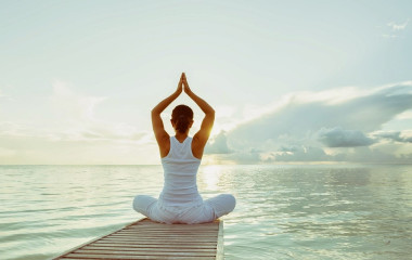 Frau praktiziert Yoga am Wasser vor dem Sonnenaufgang