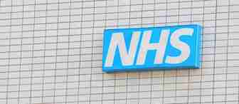 A sign with "NHS" in white letters on a blue background is mounted on a beige tiled wall.