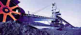 An industrial mining excavator with a large rotating wheel is extracting and moving earth. The massive machine is situated in a quarry with heaps of dirt and rock surrounding it. The scene is tinged with purple hues, creating a surreal atmosphere.