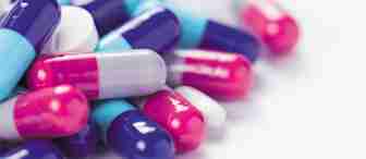 A close-up image of a pile of various pills and capsules. The capsules are predominantly in shades of blue, pink, white, and purple, while the pills are mostly white. The background is a plain, light surface.