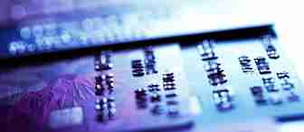 Close-up image of several credit cards laid out flat, with focus on the raised numbers of one card in the foreground. The image is illuminated with a mix of purple and blue light, giving it a modern and tech-savvy appearance.