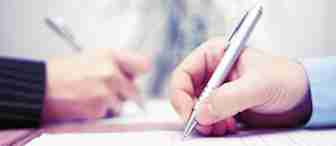 Close-up of two people writing on documents with silver pens. The focus is on their hands, one person wearing a suit jacket and the other in a light blue shirt, both engaged in what appears to be a formal signing or writing activity.