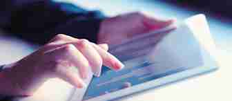 A person interacts with a tablet screen, using their index finger to touch the device. The tablet displays a chart or graph with bars, indicating data is being viewed or analyzed. The background is softly blurred, focusing attention on the hands and the tablet.