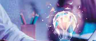 A person types on a laptop with a cup of coffee nearby. A digitally rendered, glowing light bulb made of geometric shapes floats above the laptop, symbolizing an idea or innovation. The background includes a pencil holder and blurred figures.