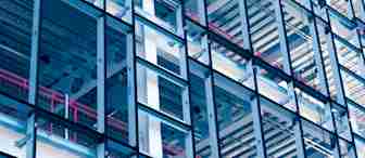 A close-up of a modern building's exterior showcasing its intricate steel framework and glass panels. Red railings and horizontal metallic elements add color and structure to the composition, creating a geometric and industrial aesthetic.