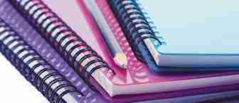 A stack of colorful spiral-bound notebooks lies on a flat surface, featuring blue, purple, and pink covers. A sharpened pencil rests diagonally across the top notebook. The notebooks are slightly askew, creating a layered, overlapping effect.